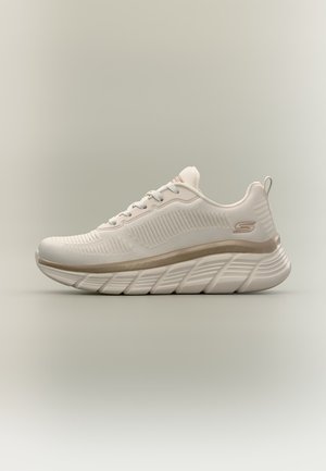 Weißer und beiger Sportschuh mit strukturiertem Stoffobermaterial, dicker gepolsterter Sohle, Schnürsenkeln und kleinem Logo an der Seite.