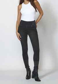 Svarta högmidjade jeans med slim fit, med silverdetaljer, fickor och nitar vid fållen, parat med en vit linne.