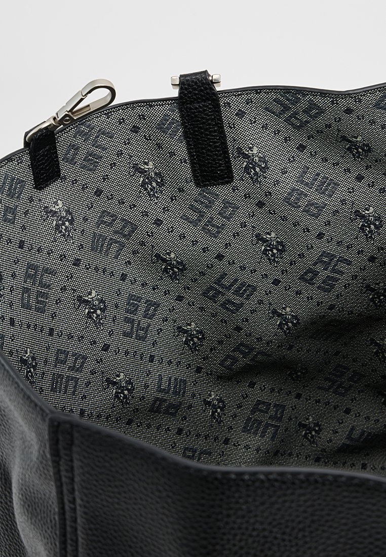 Schwarze Tote-Tasche mit einer strukturierten Außenseite und einem Innenraum mit einem geometrischen Muster in Grautönen und Marineblau. Akzentuiert mit einem Clipverschluss.