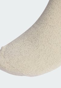 Béžová ponožka s hladkým povrchom a jemnými trblietavými vláknami. Dizajn má zaoblenú špičku a rebrovaný lem pre pohodlie.