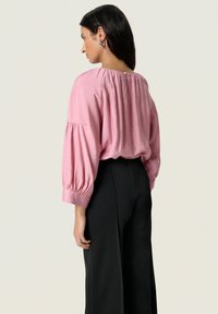 Blusa rosa a maniche corte con schiena arricciata, abbinata a pantaloni neri a gamba larga. Tessuto morbido con una vestibilità comoda.