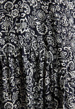 Czarna tkanina z precyzyjnym białym wzorem kwiatowym, przedstawiającym różne kwiaty i liście, marszczona przy szwie, co tworzy fakturę.