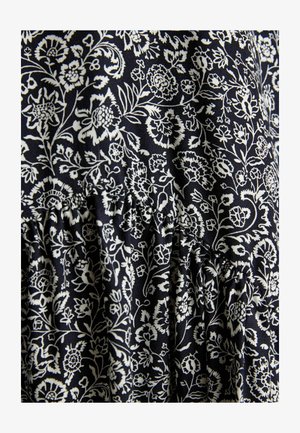 Czarna tkanina z precyzyjnym białym wzorem kwiatowym, przedstawiającym różne kwiaty i liście, marszczona przy szwie, co tworzy fakturę.