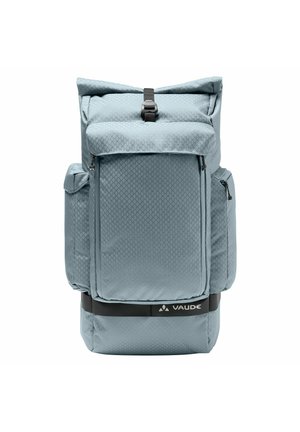 Mochila de color azul claro con cierre enrollable, bolsillos con cremallera en el frente y los laterales, correa negra ajustable y logo de Vaude en el panel inferior delantero.