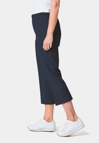 Pantalon cropped bleu marine avec une texture lisse et une taille élastique, associé à des chaussures de sport blanches dotées d'un design texturé et d'un système de laçage.
