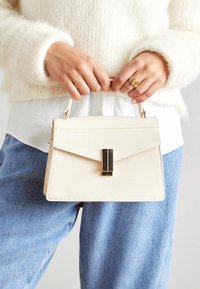 Vit texturerad handväska med en strukturerad design, som har en svart accent i hårdvara och ett kort handtag.