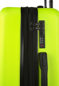 Maleta rígida verde brillante con superficie texturizada, que cuenta con dos cremalleras negras, cerradura de combinación y asa retráctil.