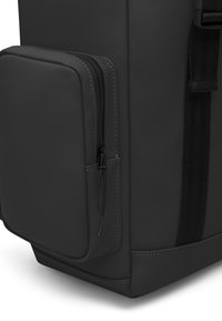 Svart ryggsäck med en jämn, matt yta, utrustad med en sidoficka med dragkedja och sömnadsdetaljer, samt ett robust tygrem.