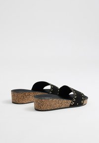 Sandalias de plataforma negras con diseño de tiras cruzadas, material de gamuza, acentos en ojetes dorados y suela de cuña de corcho texturizada.