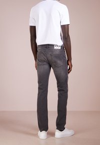 Gray denim jeans with a slim fit, featuring back pockets, a branded waistband tag, and paired with white sneakers and a white polo shirt.