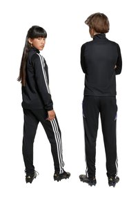 Schwarze sportliche Trainingsanzüge mit langen Ärmeln und hohem Kragen, versehen mit weißen Drei-Streifen-Akzenten an Ärmeln und Hosen. Texturiertes Gewebe.