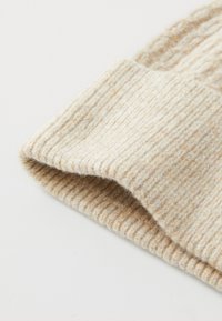 Beige ribbestrikket ullhatt med brettet kant, som viser en myk tekstur og subtile fargevariasjoner gjennom stoffet.