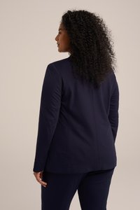 Námořnický blazer s přiléhavým střihem, hladkým materiálem, dlouhými rukávy a švy detaily. Nositý přes odpovídající kalhoty, což vytváří čistou siluetu.