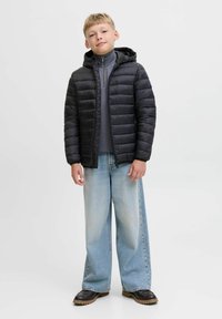 Svart puffjacka med huva, med horisontell söm. Bärs över en grå topp och kombineras med vida ljusblå jeans och svarta stövlar.