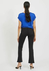 Blå kortärmad topp i kombination med högmidjade svarta utsvängda jeans, med en mjuk tygkänsla och en avslappnad passform. Svarta öppna klackar.