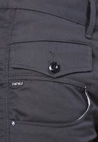 Ciemnoszare szorty z materiału z przednią kieszenią zapinaną na czarny guzik oraz przeszyciami; na kieszeni srebrne logo "RAW".