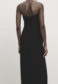 Schwarzes trägerloses Kleid mit tailliertem Oberteil, fließendem Rock und glatter Textur, mit einem verdeckten Reißverschluss auf der Rückseite.