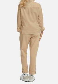 Camicia lunga beige chiaro in tessuto morbido con maniche arrotolate abbinata a pantaloni affusolati dello stesso colore e sneakers bianche.