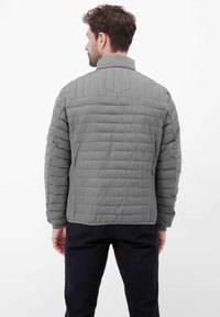 Szara pikowana kurtka z kołnierzem stójką i przeszywanymi segmentami. Charakteryzuje się gładką fakturą i elastycznymi mankietami, noszona na czarnych spodniach.