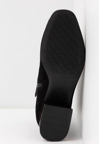 Bottine en daim noir avec un talon empilé, dotée d'une semelle en caoutchouc texturée et d'une fermeture éclair latérale pour un ajustement sécurisé. Pointure 37.