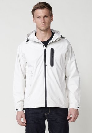 Chaqueta blanca impermeable con capucha, cremallera negra y detalles en negro. Incluye un bolsillo en el pecho con cremallera y puños ajustables. Textura suave, ligera.