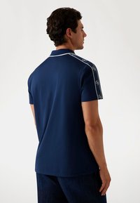 Navy-Polohemd mit kurzen Ärmeln, das weiße Kragenakzente und gemusterte Details an den Schultern aufweist, aus glattem Material gefertigt.