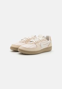 Une paire de baskets en cuir tressé beige avec des lacets blancs et un swoosh Nike blanc sur fond blanc.