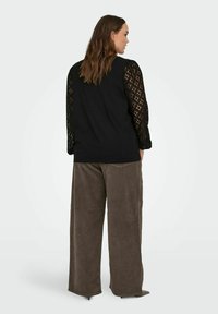 Czarna bluzka z teksturowanymi koronkowymi rękawami i gładkim korpusem, zestawiona z brązowymi, szerokimi spodniami z sztruksu. Charakteryzuje się luźnym krojem i miękkimi materiałami.