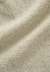 Tissu en lin beige avec un tissage texturé subtil et des plis doux créant de douces ombres sur la surface.