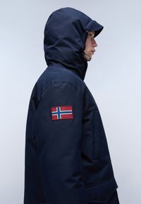 Giacca isolante blu navale con cappuccio, dotata di una patch della bandiera norvegese sul maniche sinistra e una texture liscia e resistente all'acqua.