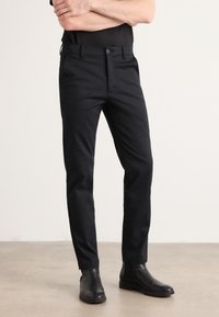 Zwarte broek met een slimme pasvorm, met een soepele textuur en een knoopsluiting. Gecombineerd met zwarte Chelsea-boots.