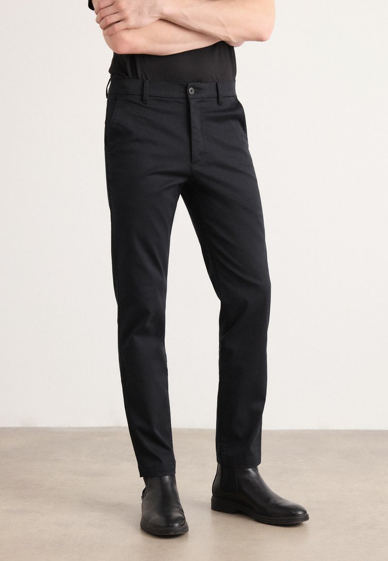 Zwarte broek met een slimme pasvorm, met een soepele textuur en een knoopsluiting. Gecombineerd met zwarte Chelsea-boots.