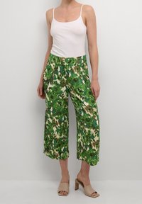 Pantaloni a gamba larga con motivo floreale verde in tessuto leggero, dotati di vita elastica e tasche, abbinati a una canotta bianca.