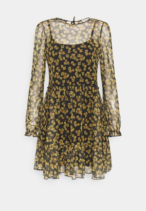 Robe longue noire transparente à manches longues avec imprimé floral jaune, encolure dégagée, ourlet à volants et jupon intérieur sans manches.