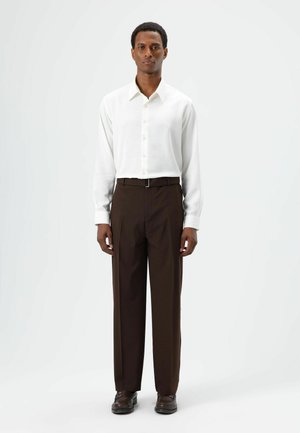 White long-sleeve shirt with a pointed collar, paired with brown trousers. The outfit features a classic fit and smooth textures.