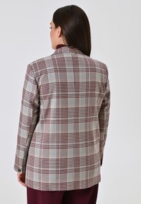 Karierter Blazer in Hellgrau mit burgunderfarbenen Akzenten, ausgestattet mit einem Reverskragen, strukturierten Schultern und einem Knopfdetail am Ärmel.