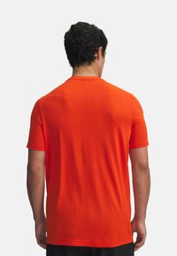 Kratek-sleevni športni majica v svetlo oranžni barvi, izdelana iz teksturirane tkanine. Na hrbtnem delu ima tonalen logotip "UNDER ARMOUR".