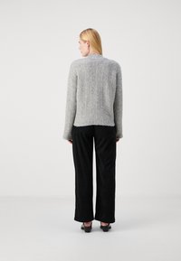 Maglione grigio lavorato a maglia con un design testurizzato, vestibilità comoda e orlo a coste. Abbinato a pantaloni neri a gamba larga e scarpe nere con tacco.