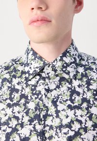 Blomstrete kortermet skjorte i marineblått har hvite og grønne mønstre, standard krage og knappestolpe-detaljer i glatt stoff.