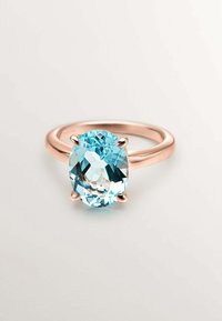 Gema de aguamarina ovalada engastada en un anillo de oro rosa. Banda lisa con cuatro garras sujetando la piedra, mostrando su claridad y color.