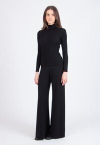 Črna rebrasta turtleneck pulover, povezana s širokimi črnimi hlačami; oba kosa imata gladko teksturo in prilagojen silhueto.