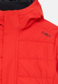 Casaco isolante vermelho com colarinho alto, apresentando textura acolchoada e um logo preto da CMP na frente. Forro interno suave visível.