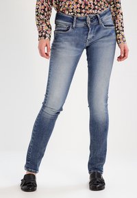 Smal passform denimjeans i ljusblått med subtila blekningar, femfickdesign och kontrasterande sömmar. Har dragkedja och knappstängning.