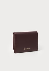 Složená tmavě hnědá kožená peněženka se zlatým logem Calvin Klein, vystavená na jednoduchém světlém pozadí.