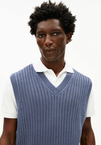 Blauw gebreid vest met verticale ribbels en een V-hals, gedragen over een wit overhemd met kraag. Heeft een gestructureerd patroon en korte mouwen.