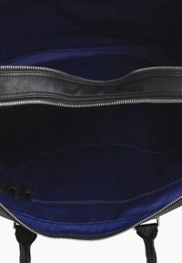 Interno di una borsa in pelle nera con rivestimento in tessuto blu navy, dotata di una cerniera argentata e di una tasca a contrasto blu. Texture liscia e cuciture ordinate.