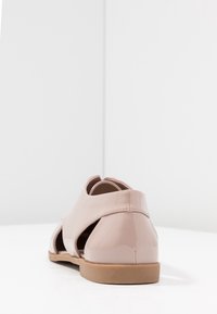 Sandale en cuir verni rose avec design découpé, semelle plate et bout arrondi. Détails de coutures au talon et construction légère.