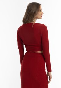 Rød, tætsiddende to-delt outfit bestående af en langærmet crop top og et højdefineret nederdel, lavet af et skinnende stof med en glat overflade.