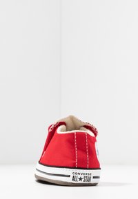Zapatilla de lona roja con diseño de corte bajo, suela de goma blanca, acentos cosidos y un parche de logo en el lado exterior.
