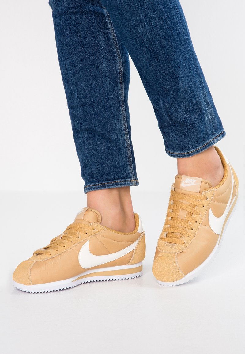 Tan Nike-sneakers har överdel i läder och mocka, vit swoosh-logga, snörning och texturerad sula. Bärs med mörka denimjeans.